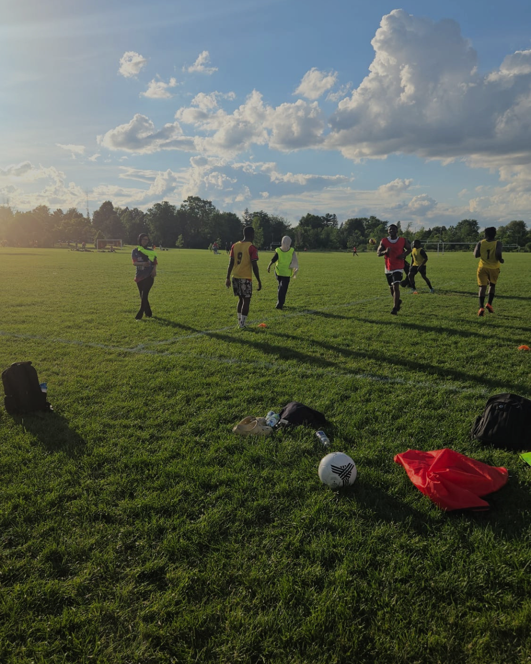 B6 Soccer Academy players training together on an outdoor grass pitch under a bright sky